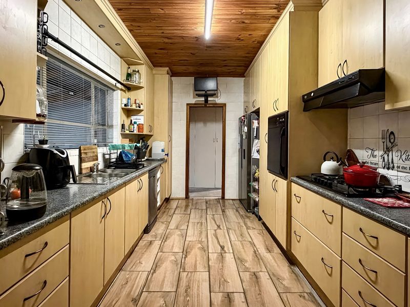 Galley-style kitchen featuring light wood cabinetry, granite-look laminate countertops, built-in oven, gas hob, and a distinctive timber-paneled ceiling.