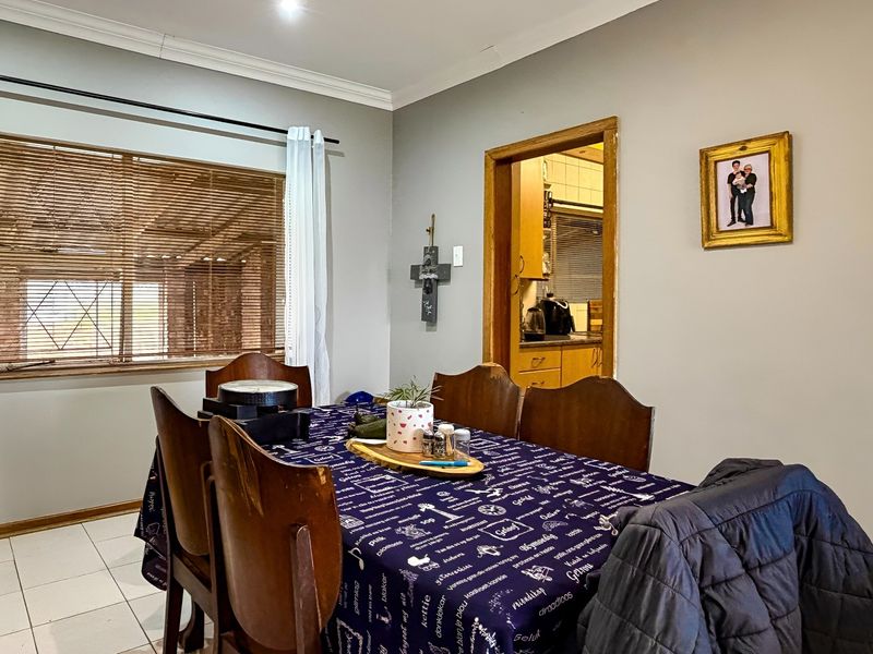 A functional dining room featuring tiled flooring and wooden blinds, with a direct view into the adjacent kitchen area.
