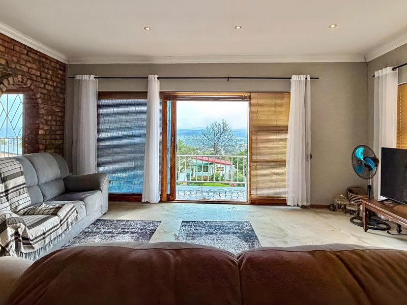 Spacious living room featuring an exposed brick feature wall, recessed lighting, and large sliding doors opening onto a balcony with scenic views.
