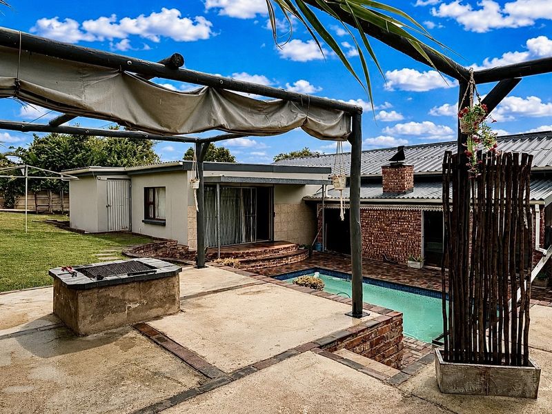 Outdoor entertainment area featuring a swimming pool, paved patio, and a built-in braai under a pergola structure.