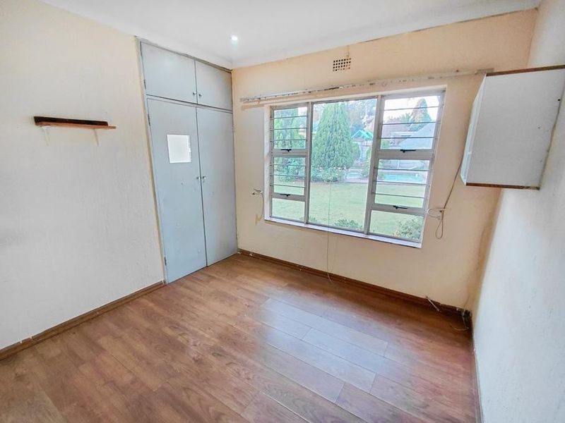 An empty bedroom featuring laminate flooring, built-in cupboards, and large steel-framed windows overlooking the garden.