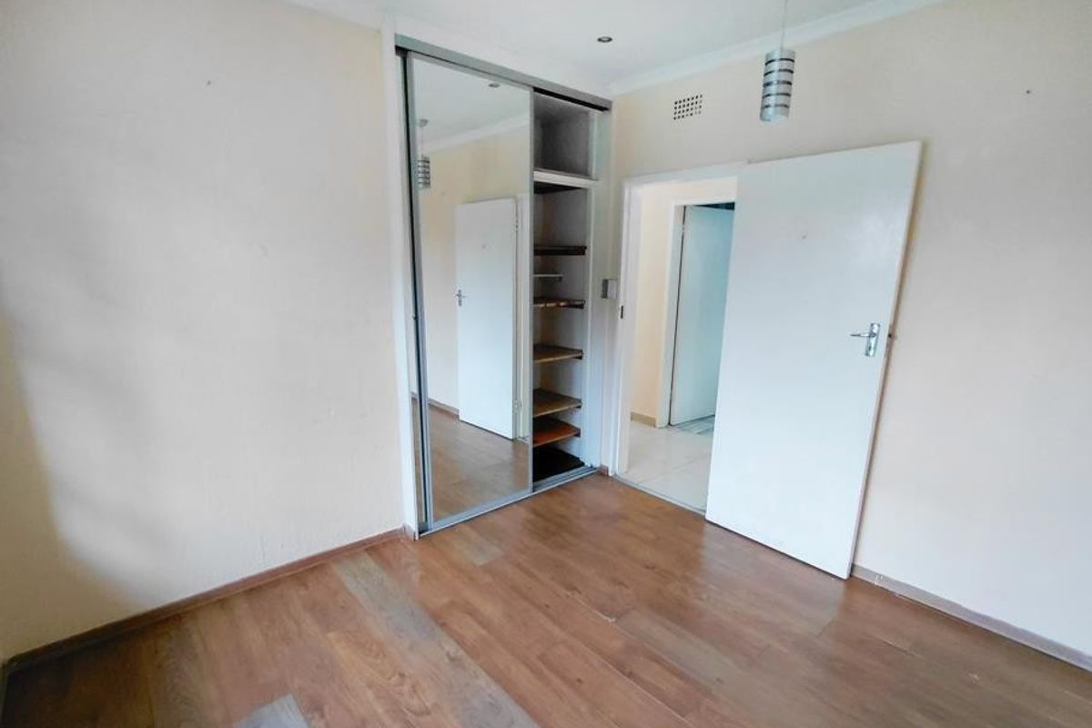 An empty bedroom featuring laminate flooring, a built-in mirrored sliding wardrobe, and neutral wall finishes.