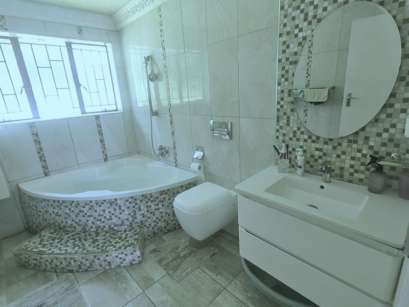 A well-appointed bathroom featuring a corner bathtub, wall-mounted toilet, and a modern vanity with mosaic tile accents.