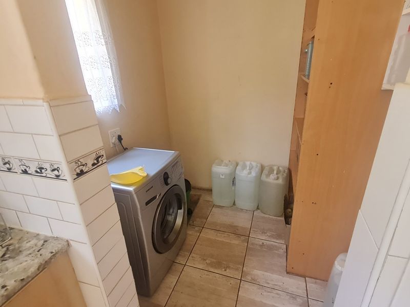 A functional laundry area featuring tiled flooring, a granite countertop, subway tile backsplash, and built-in shelving for storage.