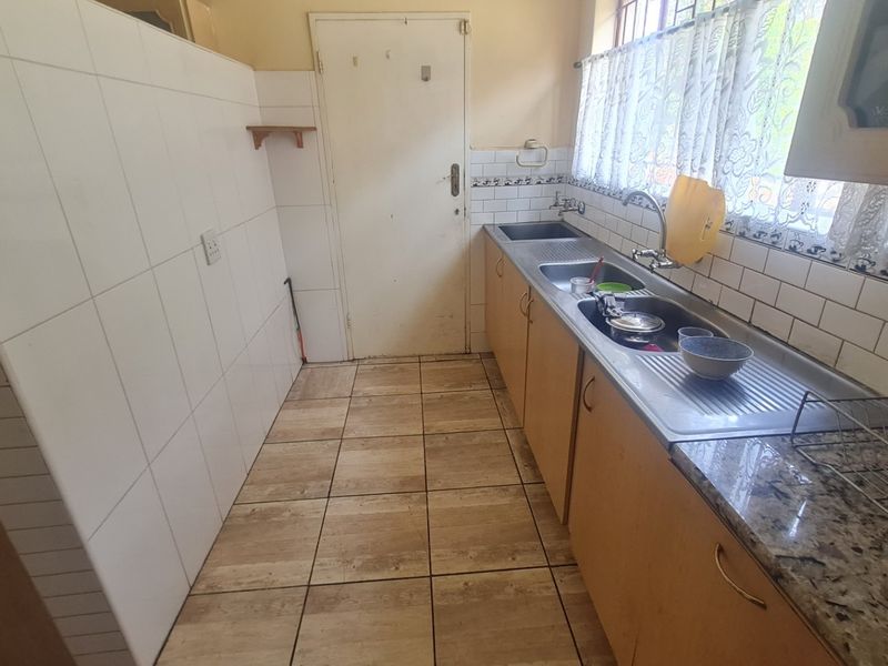 A functional kitchen featuring built-in cabinetry, granite countertops, a stainless steel sink, and tiled splashbacks with neutral floor tiles.