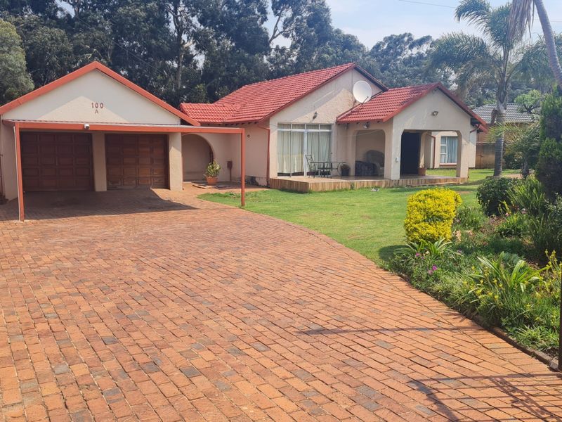 Front view of a residential house featuring a double garage, brick paved driveway, and a covered patio area with a well-maintained garden.