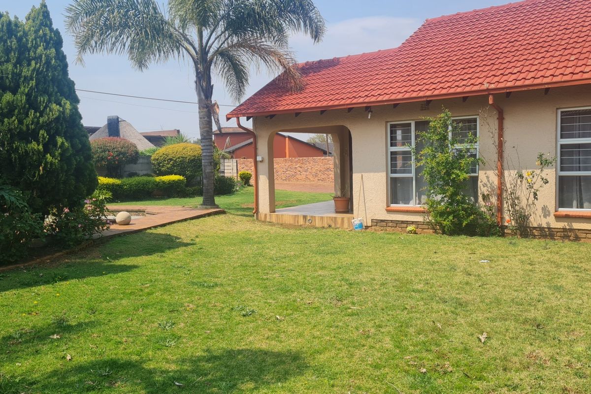 Rear view of the house featuring a covered patio, tiled roof, and a well-maintained garden with lawn and established trees.