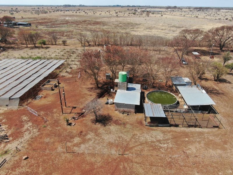 Aerial view of farm infrastructure including a circular reservoir, water storage tank, and large shade netting structures on a rural property.