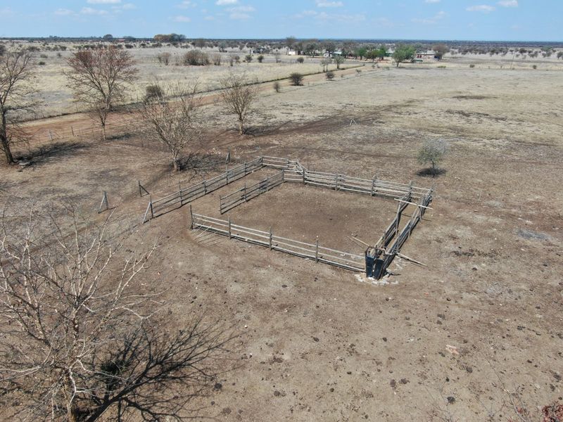 Aerial view of a farm property featuring a livestock kraal with wooden fencing and a cattle crush set in an open field.