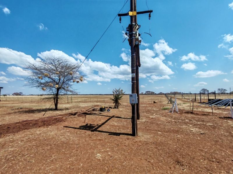 Open farm land featuring a utility pole with electrical infrastructure and perimeter wire fencing under a clear sky.