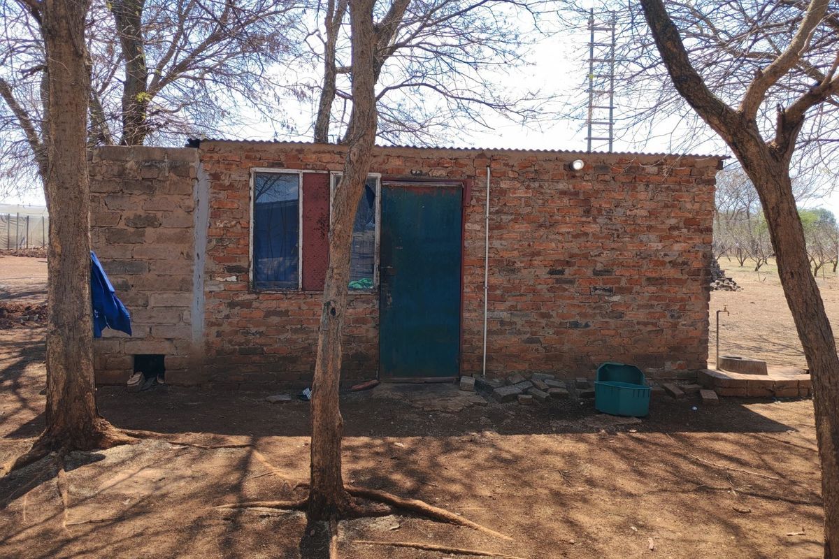 A rustic farm outbuilding featuring exposed brick construction, a metal door, and a corrugated iron roof, situated in a natural, tree-lined outdoor setting.