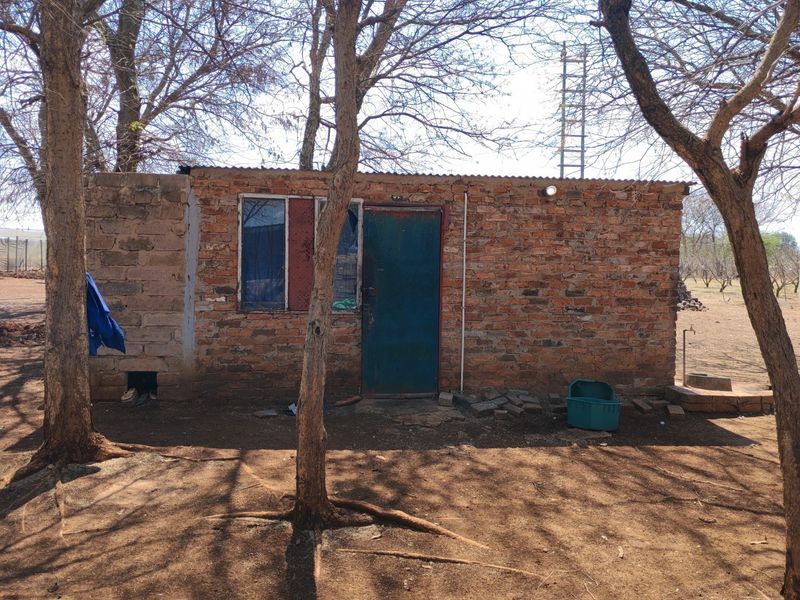A rustic farm outbuilding featuring exposed brick construction, a metal door, and a corrugated iron roof, situated in a natural, tree-lined outdoor setting.