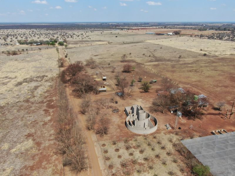 Aerial view of a large farm property featuring an unfinished circular concrete structure, outbuildings, and an orchard set within a rural landscape.