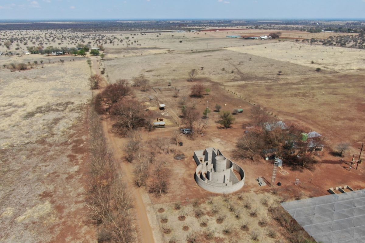 Aerial view of a large farm property featuring an unfinished circular concrete structure, outbuildings, and an orchard set within a rural landscape.
