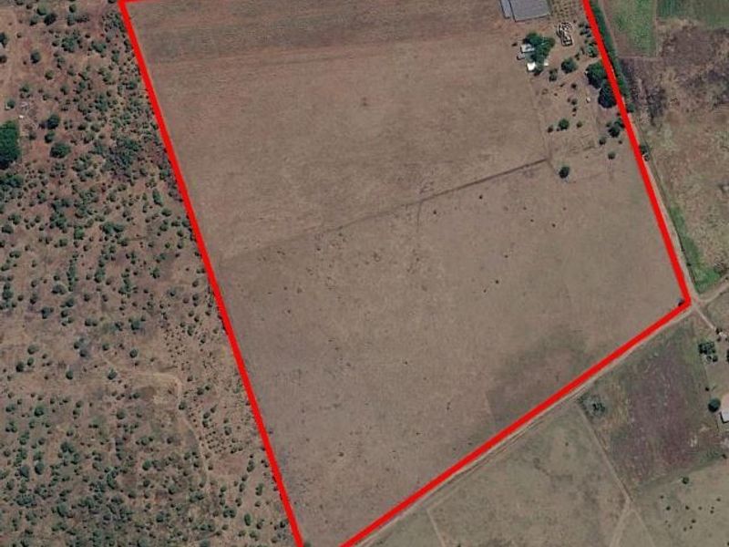 Aerial view of a large farm property with a clearly marked boundary, featuring open grazing land and existing outbuildings.