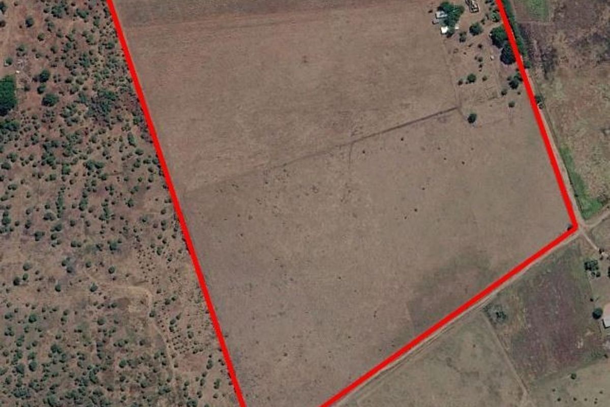 Aerial view of a large farm property with a clearly marked boundary, featuring open grazing land and existing outbuildings.