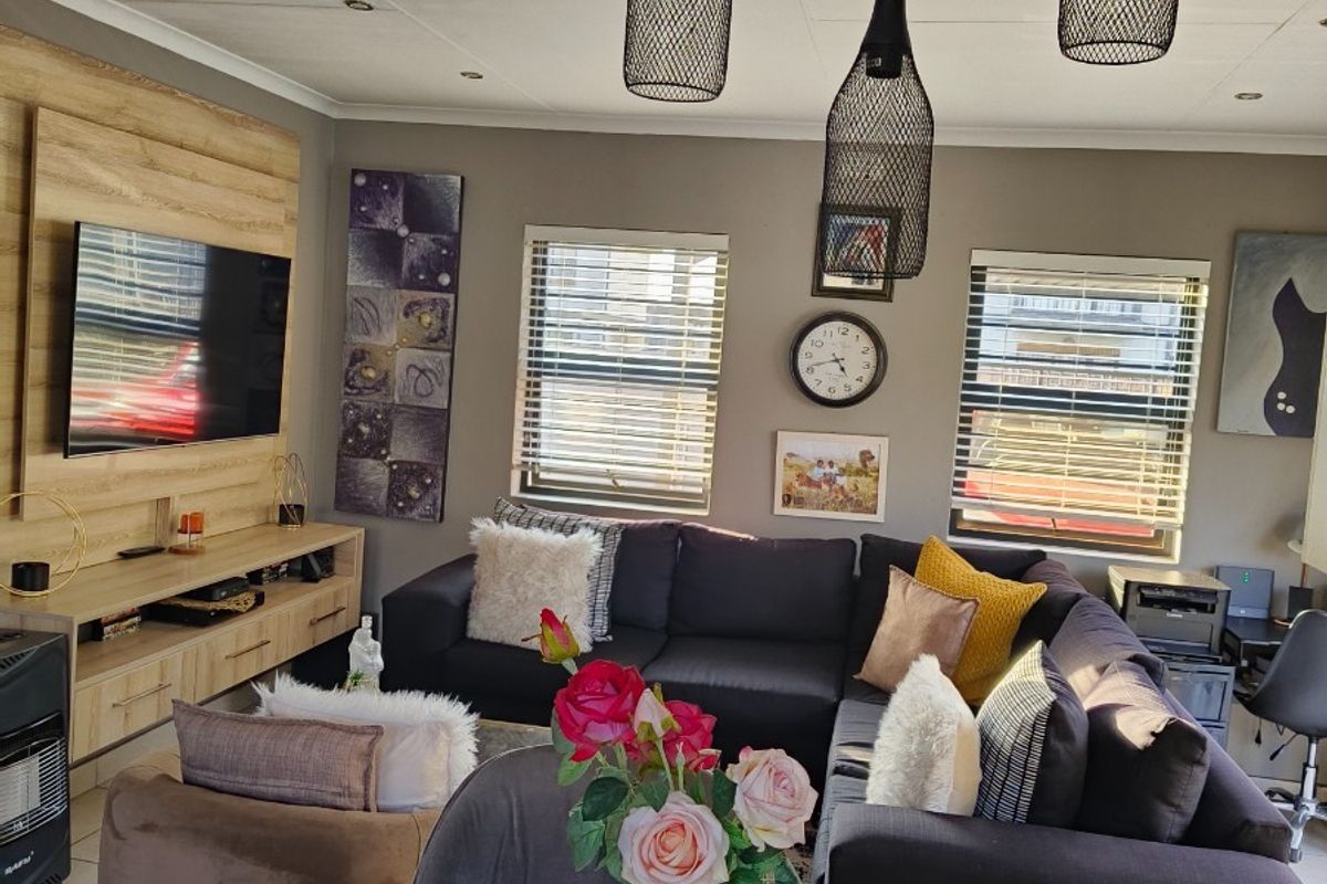 A well-lit living room featuring tiled flooring, modern pendant lighting, venetian blinds, and a built-in media unit.