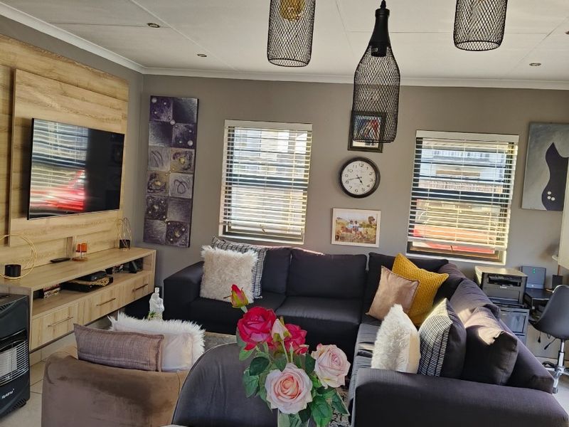 A well-lit living room featuring tiled flooring, modern pendant lighting, venetian blinds, and a built-in media unit.
