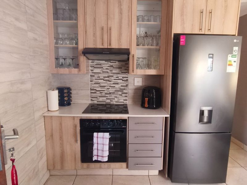 A compact, modern kitchen featuring light wood-finish cabinetry, stone countertops, a tiled splashback, and integrated cooking appliances.