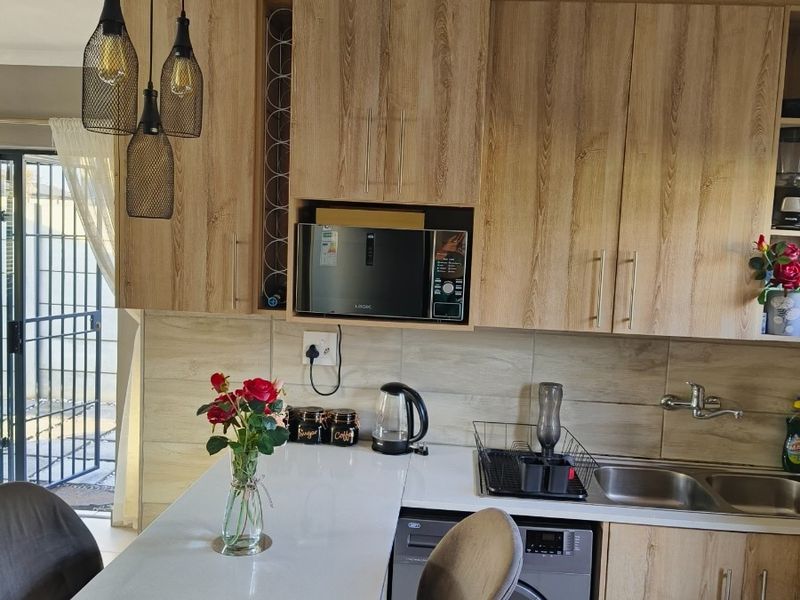 A modern kitchen featuring light wood-grain cabinetry, white countertops, a built-in microwave, and a convenient integrated washing machine with a breakfast bar area.