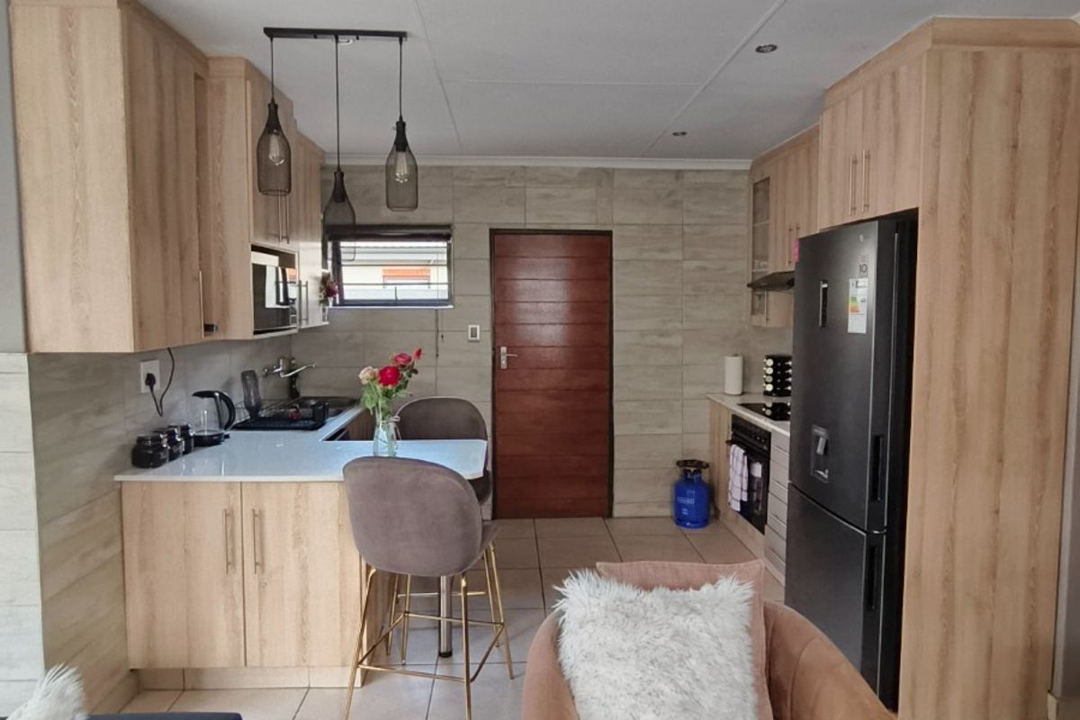 Modern kitchen featuring light wood cabinetry, stone countertops, integrated appliances, and tiled flooring, creating a functional and contemporary cooking space.