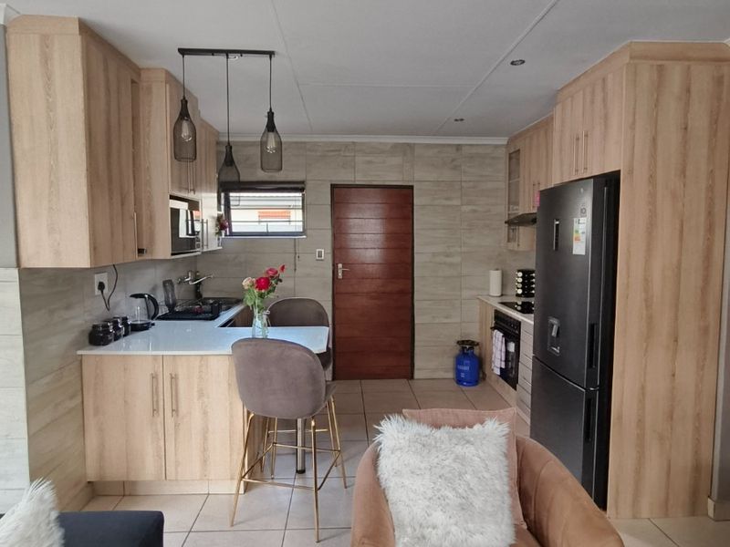 Modern kitchen featuring light wood cabinetry, stone countertops, integrated appliances, and tiled flooring, creating a functional and contemporary cooking space.