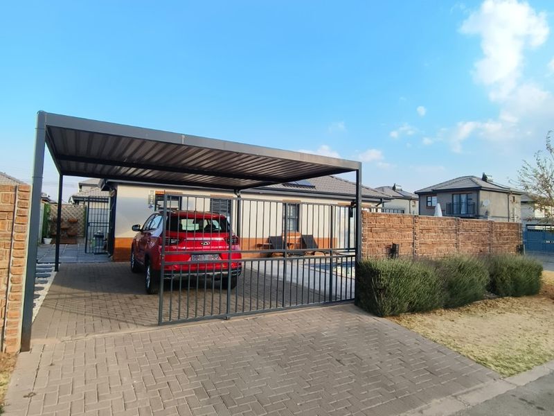 Front exterior view featuring a paved driveway, a modern metal carport, and secure perimeter brick walling with a metal gate.