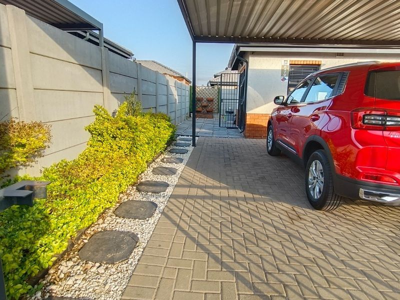 A well-maintained front exterior featuring a paved driveway, a covered carport, and a neat garden path alongside a precast boundary wall.