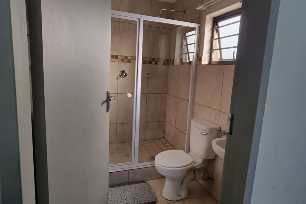 A functional bathroom featuring a shower enclosure, toilet, and wash basin with neutral wall and floor tiling.