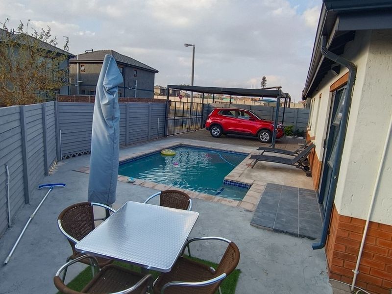 Outdoor pool area featuring a paved patio, perimeter fencing, and an adjacent carport, providing a functional space for outdoor relaxation and parking.