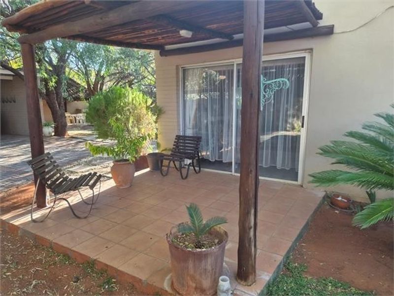 A covered patio area featuring tiled flooring and a rustic timber pergola, providing direct access to the interior through a sliding glass door.