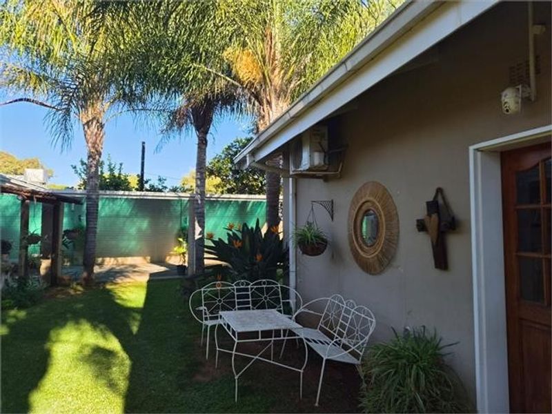 A view of the rear exterior of the house featuring a lawn, mature palm trees, and a paved area adjacent to the building wall.