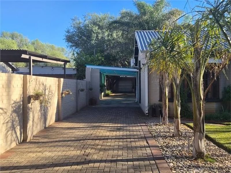 A paved driveway leading to a carport, featuring a brick boundary wall and established garden landscaping alongside the main house structure.