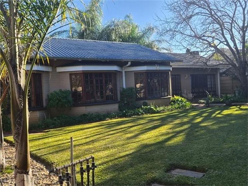 Rear view of the house featuring a metal roof, bay windows with timber frames, and a well-maintained garden area.