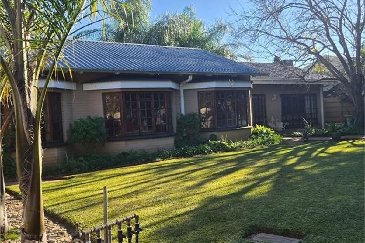 Rear view of the house featuring a metal roof, bay windows with timber frames, and a well-maintained garden area.