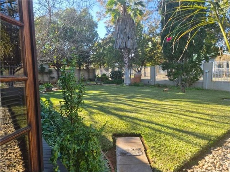 A well-maintained private garden featuring a lush green lawn, mature trees, and a secure perimeter wall with a paved walkway.