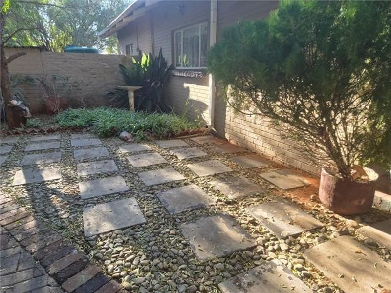 A rear garden area featuring a brick wall, paved stepping stones, and pebble landscaping adjacent to the house exterior.