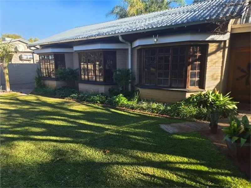 Rear view of the house featuring a corrugated metal roof, brick exterior, and multiple bay windows overlooking a well-maintained garden.