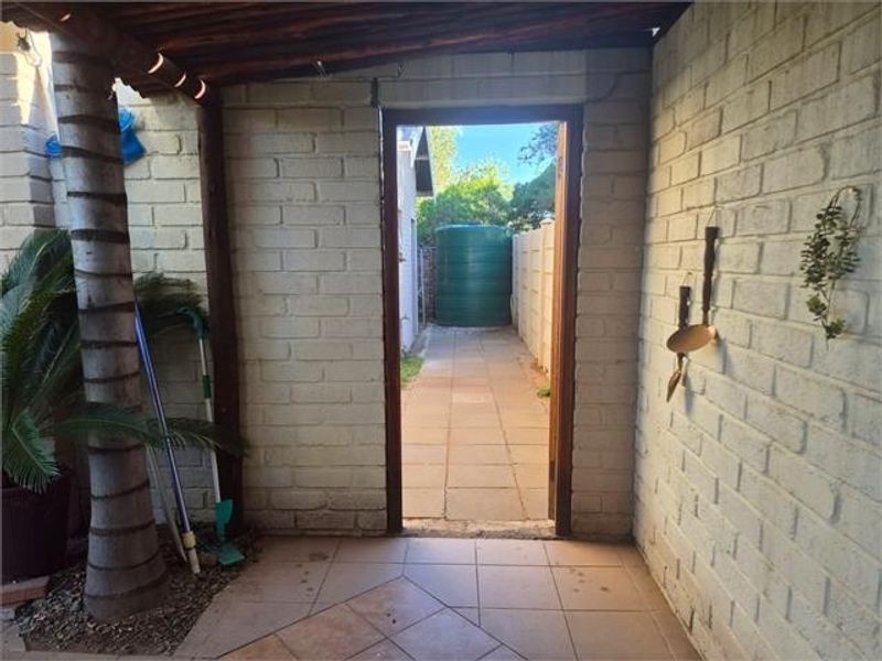 A covered outdoor patio area featuring brick walls and tiled flooring, providing access to a side garden path with a water tank.