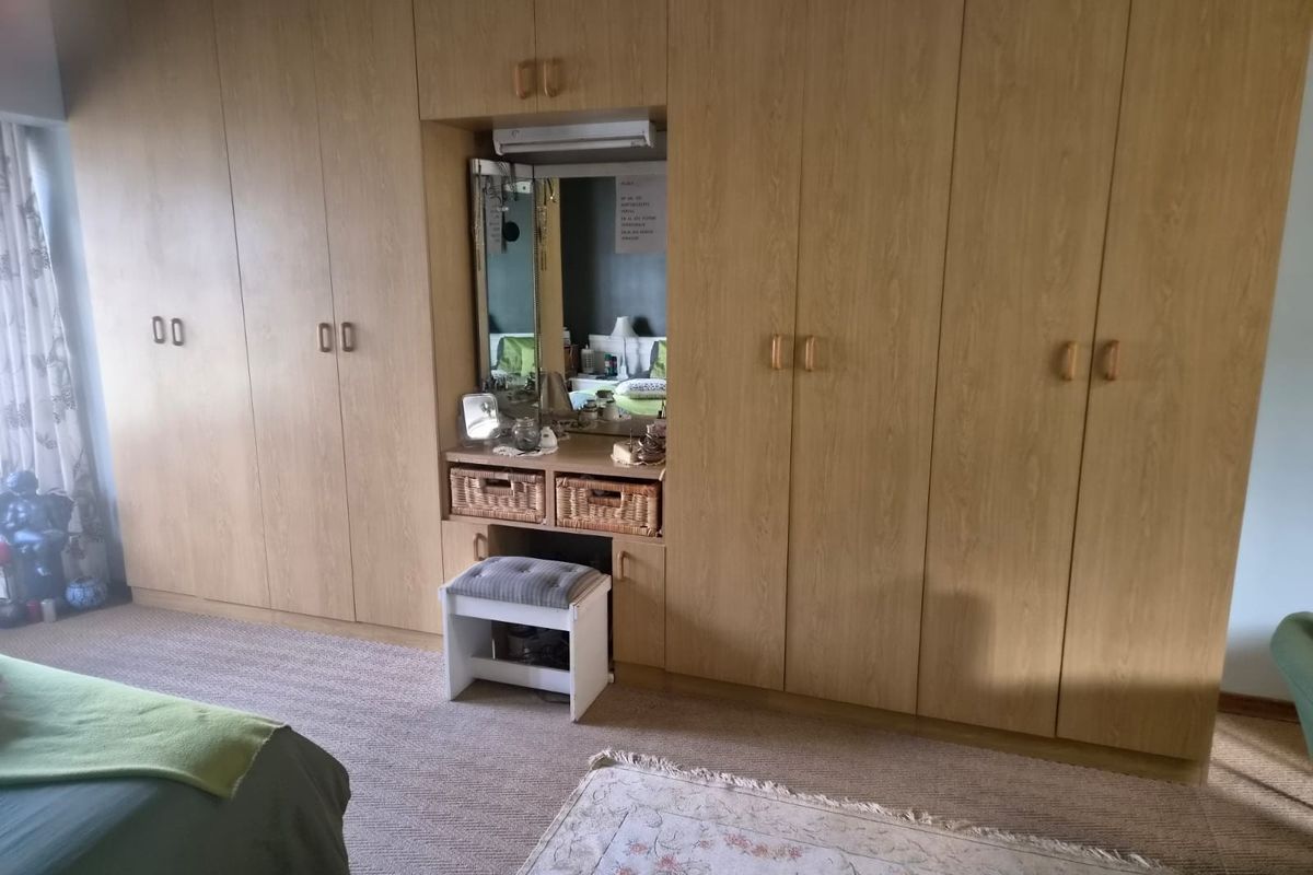 A bedroom featuring extensive wall-to-wall built-in wooden cupboards with an integrated vanity area and mirror.