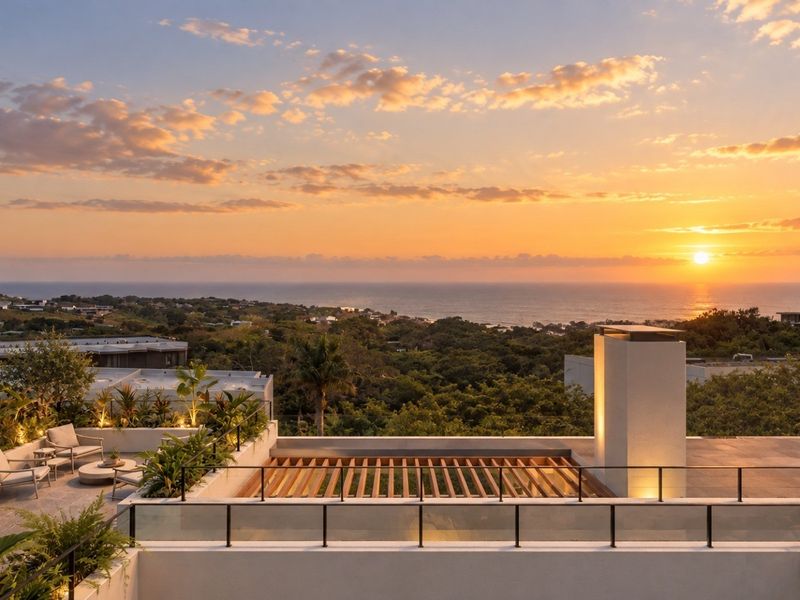 A stunning rooftop terrace featuring a timber pergola, masonry chimney, and glass-panelled railings, offering panoramic sunset views over the coastline.