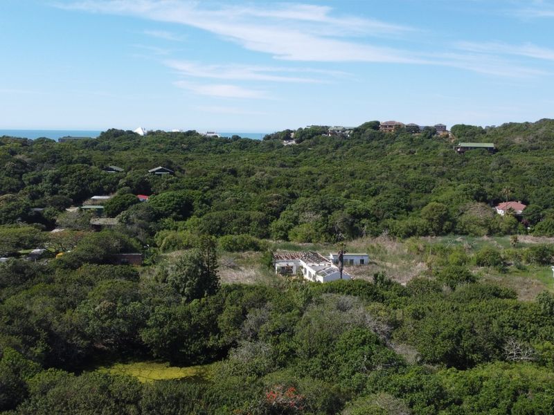 An aerial view of a residential plot surrounded by dense coastal vegetation and natural landscape.