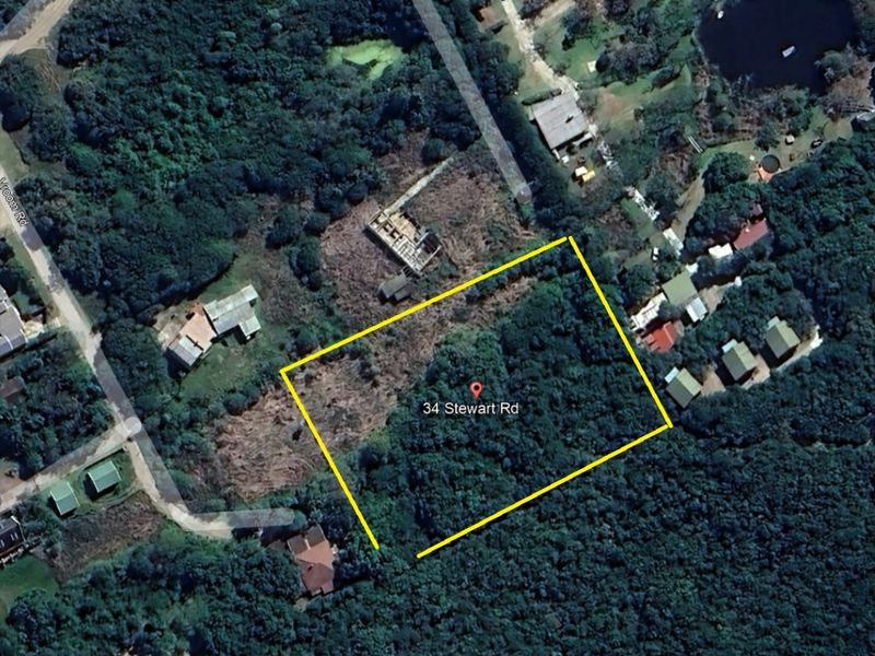An aerial view of a vacant residential plot of land surrounded by dense vegetation and nearby residential properties.