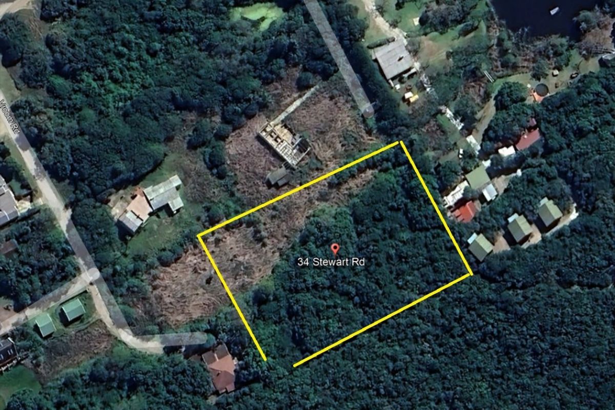 An aerial view of a vacant residential plot of land surrounded by dense vegetation and nearby residential properties.