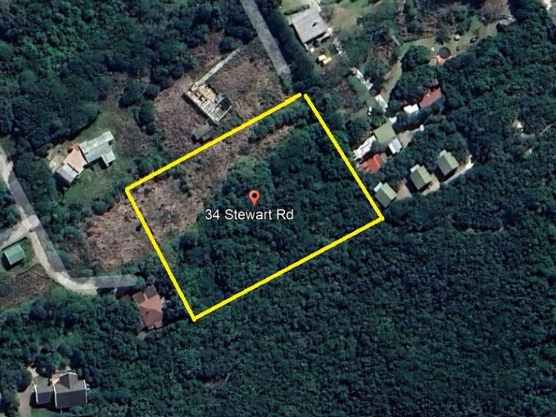 Aerial view of a vacant residential plot marked with a yellow boundary line, surrounded by dense natural vegetation and nearby residential properties.