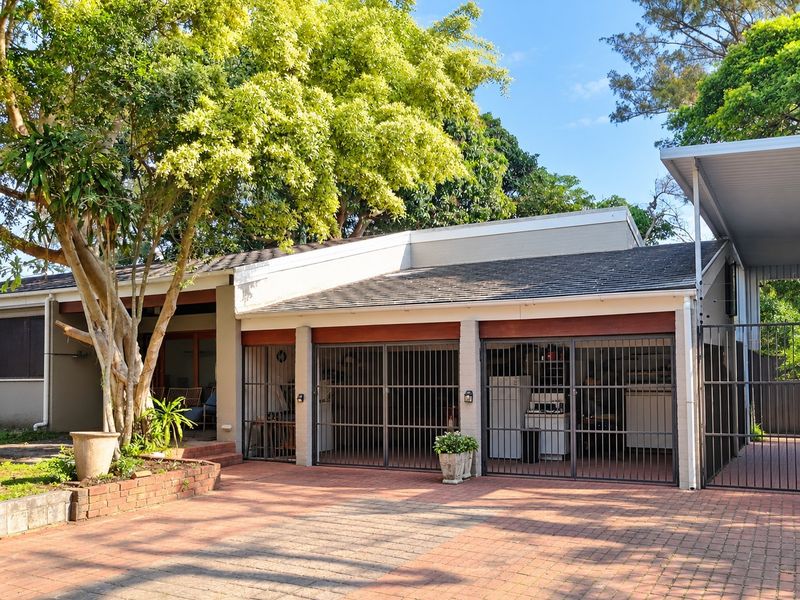 Front exterior view of the property featuring a brick paved driveway, triple garage with security gates, and an attached carport.