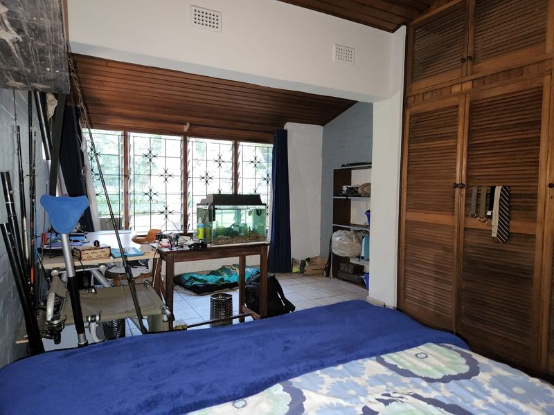 Bedroom featuring a timber-paneled ceiling, tiled flooring, and extensive built-in timber wardrobe storage with security bars on the windows.