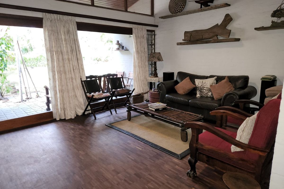 Spacious living room featuring dark parquet flooring, exposed brick walls, and large sliding glass doors that provide seamless access to the outdoor patio area.