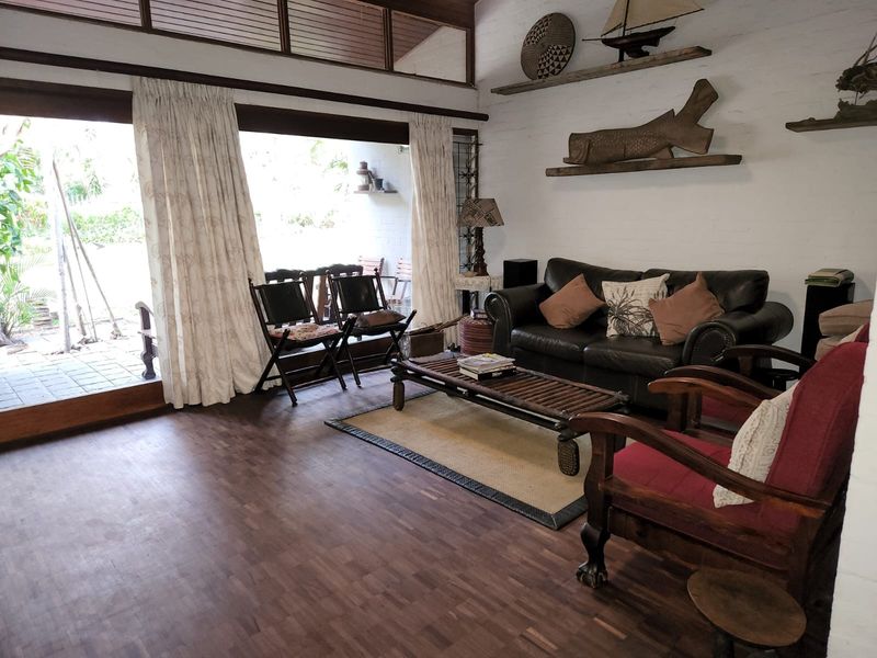 Spacious living room featuring dark parquet flooring, exposed brick walls, and large sliding glass doors that provide seamless access to the outdoor patio area.