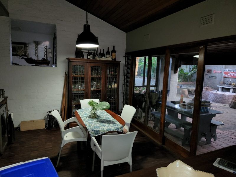 Dining area featuring exposed timber ceilings, painted brick walls, and large sliding glass doors providing direct access to the outdoor patio space.